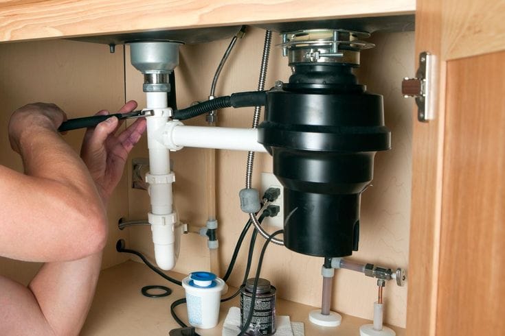 Plumber installing a garbage disposal beneath a kitchen sink in Jacksonville Beach